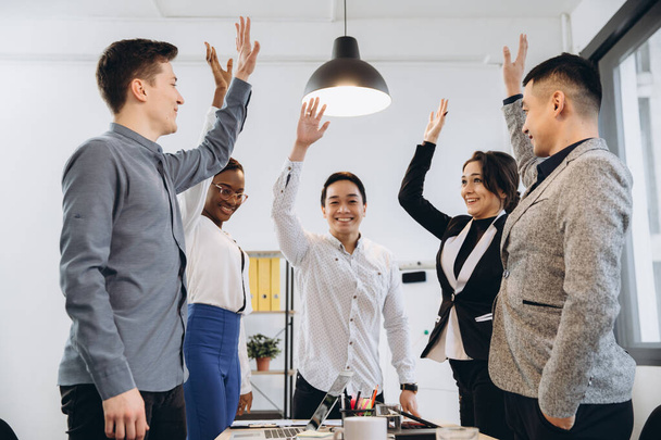 Multiracial euphoric business team people give high five at office table, happy excited diverse work group engaged in teambuilding celebrate corporate success win partnership power teamwork concept - Foto, imagen