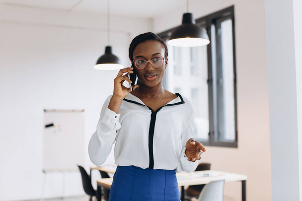 Όμορφη αφρικανή εταιρικός εργαζόμενος μιλάει στο κινητό τηλέφωνο στο σύγχρονο γραφείο - Φωτογραφία, εικόνα
