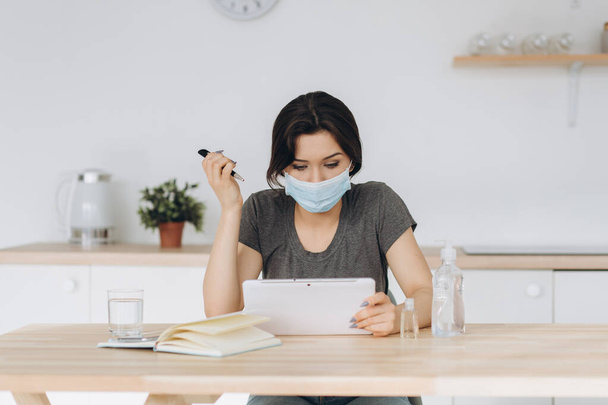 Coronavirus. Young business woman working from home wearing protective mask. Girl in quarantine for coronavirus wearing protective mask. Working from home with sanitizer gel and water - Photo, Image