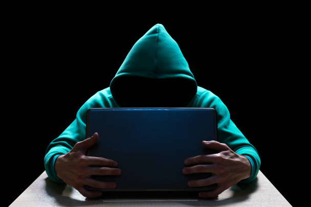 Unknown person in the hood, reaches out from the darkness to the laptop. Theft of household and computer equipment. - Foto, Imagem