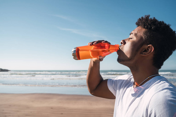 Portrait of an athletic man drinking something after training at the beach. Sport and health lifestyle. - Foto, imagen