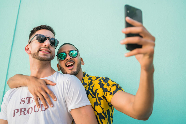 Portrait of happy gay couple spending time together and taking a selfie with mobile phone. Lgbt and love concept. - Fotó, kép