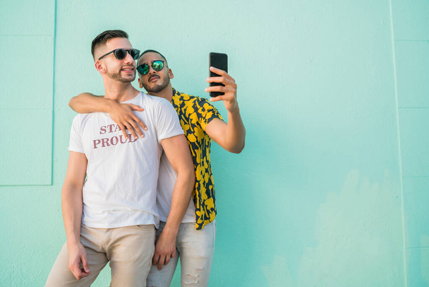 Portrait of happy gay couple spending time together and taking a selfie with mobile phone. Lgbt and love concept. - Fotó, kép