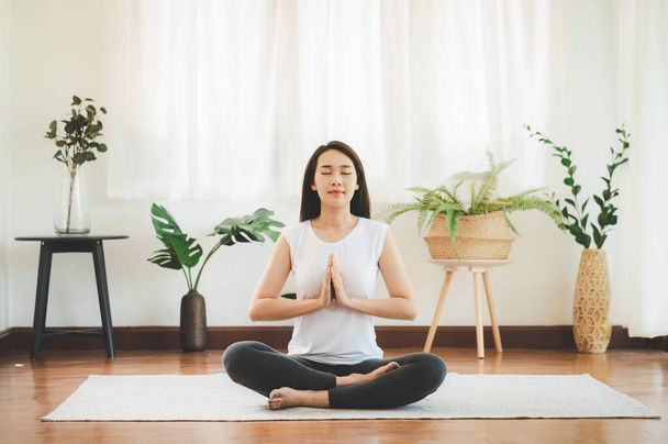 Tiro de atraente mulher asiática saudável fazendo meditação de ioga em casa na sala de estar
 - Foto, Imagem