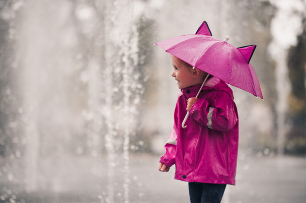 Szczęśliwe dziecko dziewczyna 4-5 lat gospodarstwa różowy parasol noszenie płaszcz przeciwdeszczowy nad deszczem w tle na zewnątrz. Jesienny sezon. Dzieciństwo.  - Zdjęcie, obraz