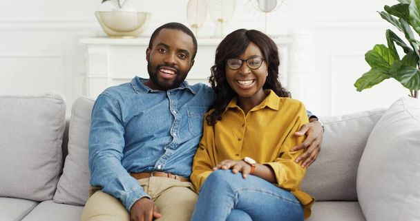 Happy African American couple husband and wife sitting on sofa looking at camera at home. - Foto, Imagen