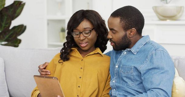 Happy African American couple husband and wife sitting on sofa using tablet and credit card for online shopping at home. - Photo, image
