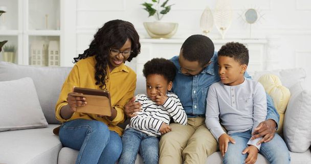 Happy African American family sitting on sofa using tablet at home. - Foto, afbeelding