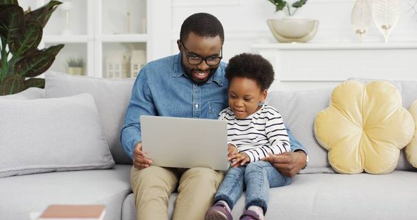 Portrait of african american father sitting with daughter on sofa using laptop watching video. - Valokuva, kuva
