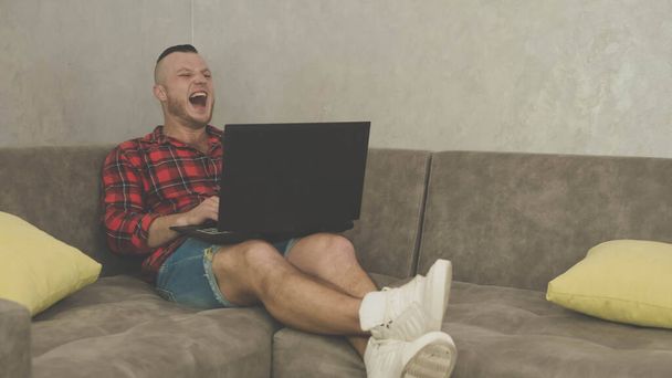 Cheerful man,guy, with a laptop on his feet,sitting on the sofa,smiling.Close-up - Foto, Imagen