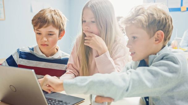 Elementary School Classroom: Diverse Group of Brilliant Children Using Laptop Computer for Software Programming, Talking and Working as a Team. Kids Learning Software Design and Creative Thinking - Фото, изображение