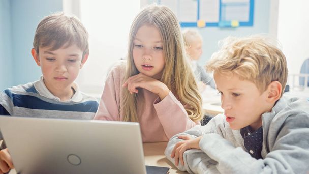 Elementary School Classroom: Diverse Group of Brilliant Children Using Laptop Computer for Software Programming, Talking and Working as a Team. Kids Learning Software Design and Creative Thinking - 写真・画像