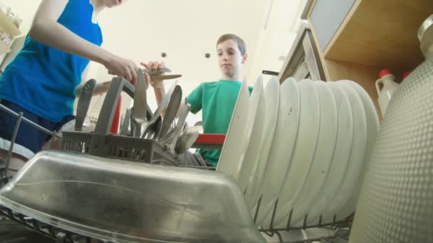Két gyerek megtölti a mosogatógépet piszkos edényekkel. - Felvétel, videó