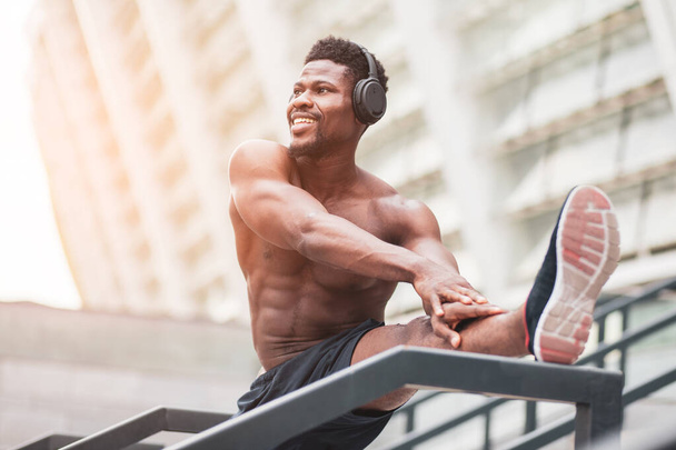 Afrikaans amerikaanse atleet training buiten tegen muur achtergrond, man met atletisch lichaam doet opwarmen en kijken naar kopieerruimte, gezonde levensstijl concept - Foto, afbeelding