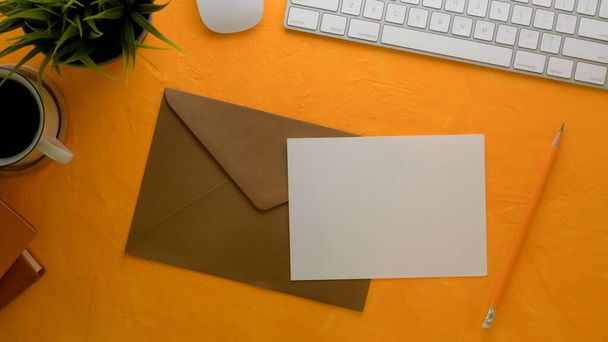 Top view of mock-up greeting card with brown envelope on creative worktable with computer keyboard and decorations - Photo, Image