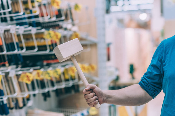 The buyer in the hardware store selects the goods. A man holds a wooden construction hammer in his hand - Foto, Imagem