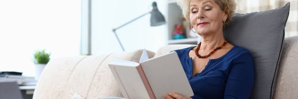 Donna anziana si siede sul divano a casa e legge libro
 - Foto, immagini