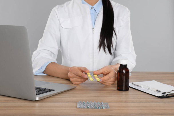 Professional pharmacist with pills and laptop at table against light grey background, closeup - Φωτογραφία, εικόνα
