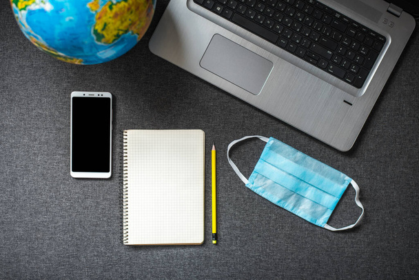 Вид зверху на ноутбук, смартфон, блокнот, глобус та медичну маску на сірому фоні. Концепція роботи з дому в самоізоляції, туристичному бізнесі або екскурсії по відпустці
 - Фото, зображення