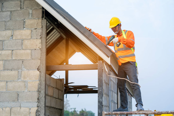 Dekarz pracujący na konstrukcji dachu budynku na placu budowy, Robotnik instalujący dach metalowy na dachu nowego domu. - Zdjęcie, obraz