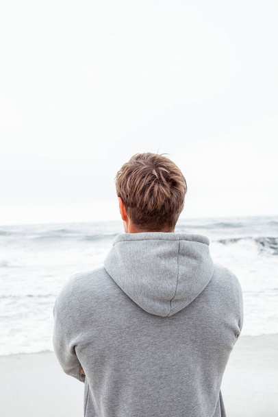 Widok z tyłu mężczyzny w szarej bluzie. Mężczyzna podziwia piękny zachód słońca na plaży. Pojęcie rekreacji, relaksu, turystyki i medytacji - Zdjęcie, obraz