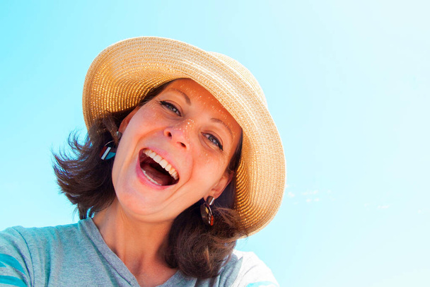 Portret pięknej młodej brunetki w słomkowym kapeluszu na tle błękitnego nieba w słoneczny dzień. Pojęcie relaksu, szczęścia i zdrowego stylu życia. - Zdjęcie, obraz