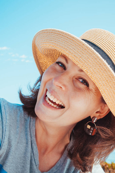 Портрет красивої молодої брюнетки в солом'яному капелюсі на тлі блакитного неба в сонячний день. Концепція розслаблення, щастя і здорового способу життя
. - Фото, зображення
