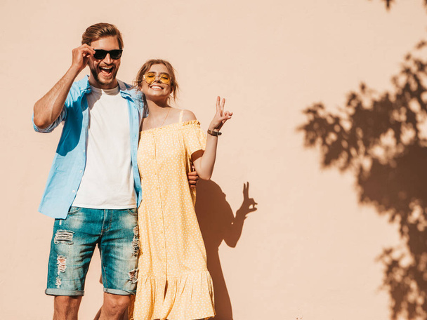 Portrait of smiling beautiful girl and her handsome boyfriend. Woman in casual summer dress and man in jeans. Happy cheerful family. Female having fun in the street near wall - Photo, image