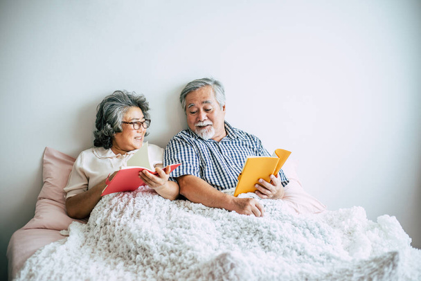Пожилая пара, лежащая на кровати и читающая книгу
 - Фото, изображение