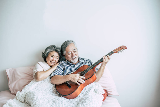 Idős pár pihenni játszani akusztikus gitár a hálószobában - Fotó, kép