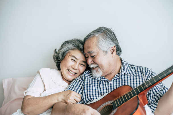 Senioren paar ontspannen spelen akoestische gitaar in slaapkamer - Foto, afbeelding