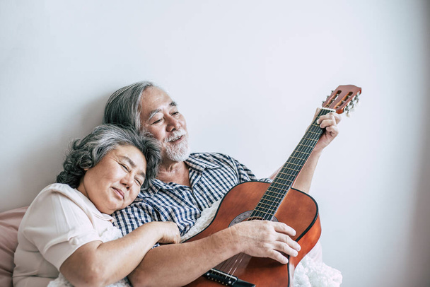 Senioren paar ontspannen spelen akoestische gitaar in slaapkamer - Foto, afbeelding