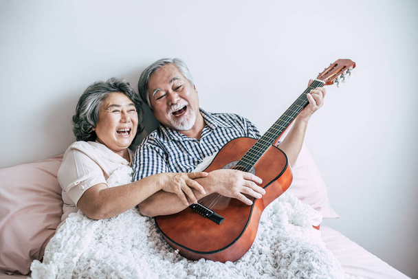Старша пара розслабляється граючи акустичну гітару в кімнаті для ліжок
 - Фото, зображення