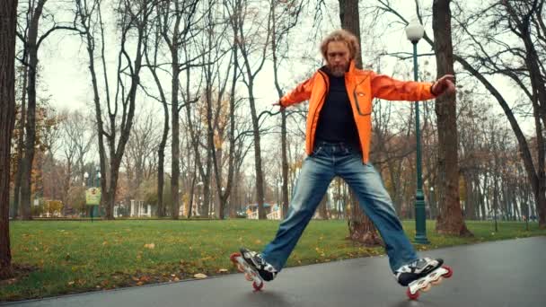 Közelkép a szakállas férfi görkorcsolyázó narancssárga dzsekiben, ügyesen korcsolyázik és komplex kanyarokat és trükköket végez a városi park sikátorában fák között. Szakmai korcsolyázó szabadtéri tevékenységeket végez - Felvétel, videó