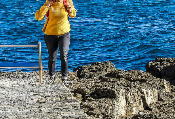 Mujer en blusa amarilla saliendo de la playa en las rocas
 - Foto, imagen