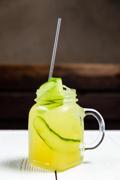 A refreshing summer lemonade with cucumber in a jar, on white wooden table - Фото, изображение