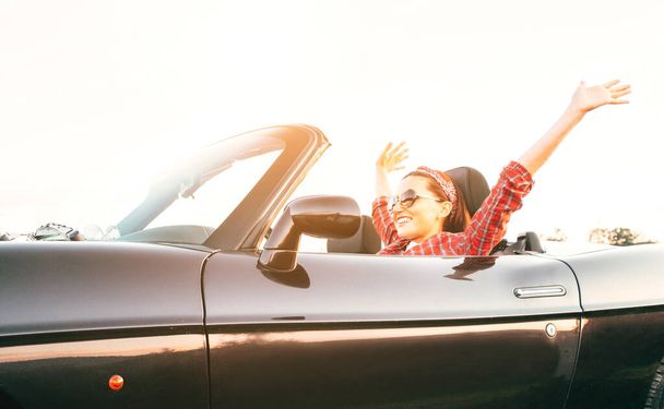 Young laughing female cheerful rising hands up in by cabriolet car in sunny day time - Photo, Image