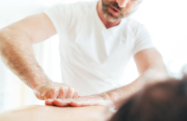 Bearded Masseur man doing massage manipulations on the Scapula area zone during young female body massaging. - Φωτογραφία, εικόνα
