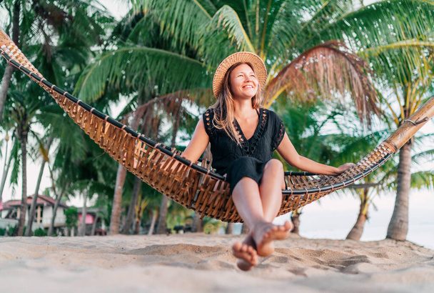 Positive young woman sitting in hammock on the tropical palm beach - Фото, зображення