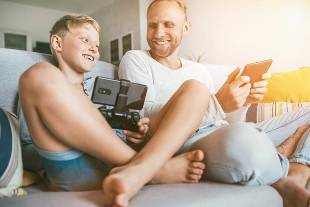 Father and son PC games fans play together with electronic devices, sit in living room - Foto, afbeelding