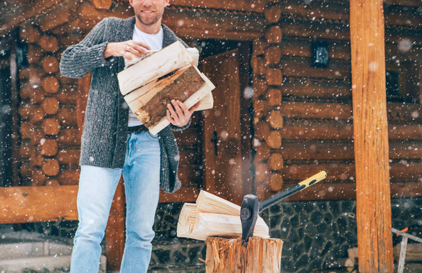 Man chopping wood on snowy yard for a house fireplace with heavy snowflakes background . Winter countryside holidays concept image - Фото, зображення