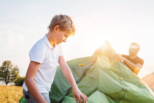 Father helps his son setting tent on sunset forest glade - Fotografie, Obrázek