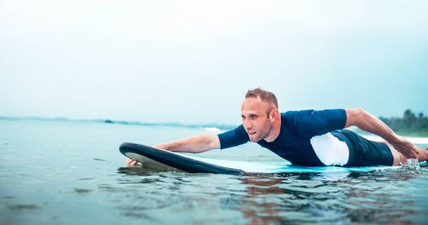Mann polstert sich auf dem Surfbrett auf. Aktives Urlaubskonzept.  - Foto, Bild