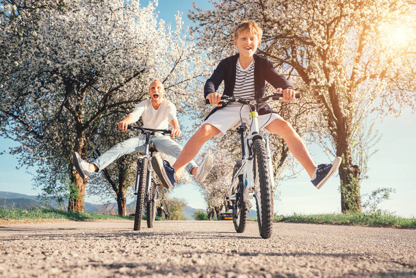 Father and son have a fun when riding bicycles on country road with blossom trees - Фото, зображення
