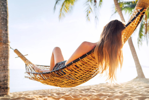 Blonde longhaired woman relaxing in hammock hinged between palm trees on the sand beach  - Fotoğraf, Görsel