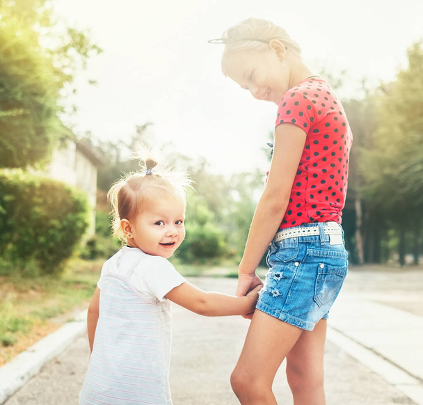Two little sisters walking together in summer city park. Family values concept photo. - Fotoğraf, Görsel