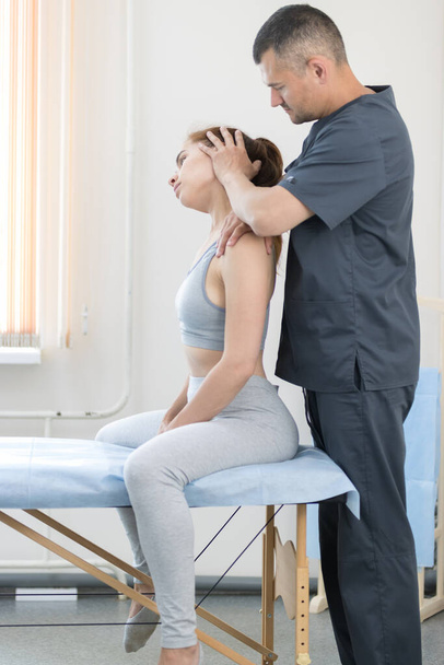 Jovem tendo tratamento de osteopatia mulher sentada no sofá e o mestre ajusta o pescoço
 - Foto, Imagem