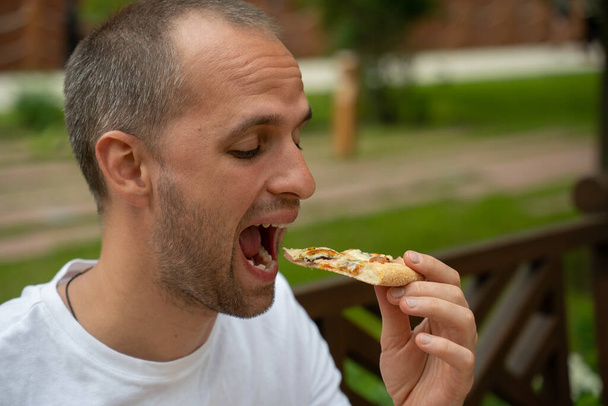 Handsome young man eating a slice of pizza in street - Foto, Imagem