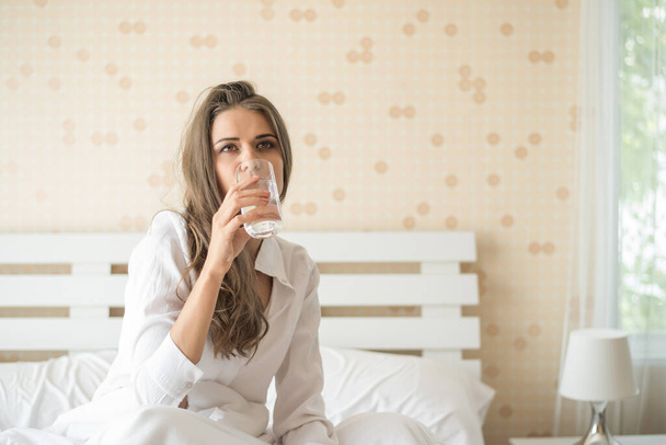 Όμορφη γυναίκα πίνει φρέσκο νερό στο κρεβάτι το πρωί - Φωτογραφία, εικόνα
