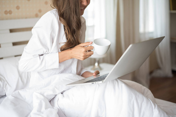 Счастливая женщина работает на ноутбуке на кровати в доме
 - Фото, изображение